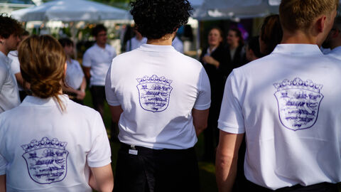 Drei Menschen stehen mit dem Rücken zur Kamera und tragen ein Hessen-Shirt